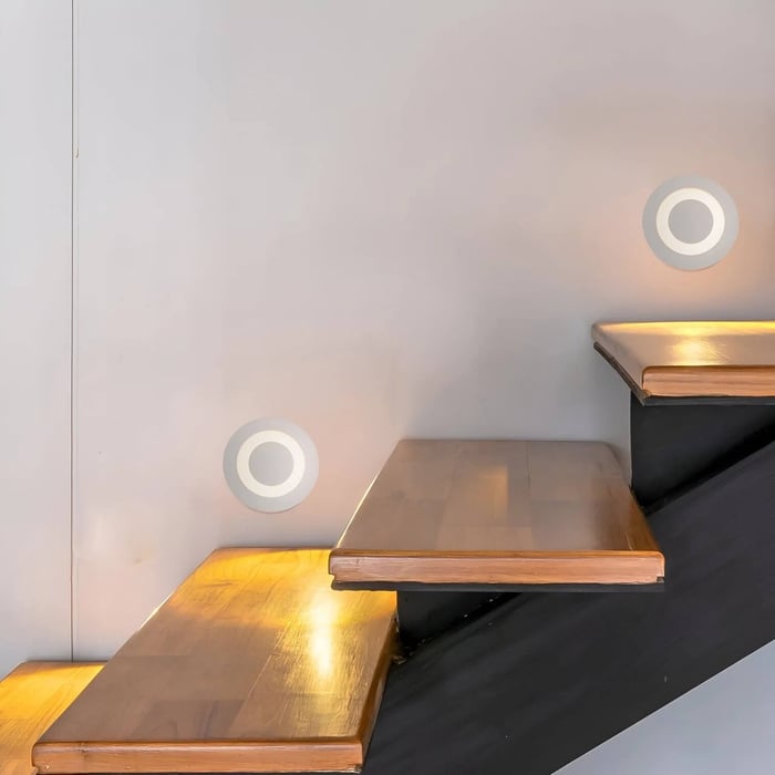 Indoor wooden stairs with round recessed wall lights producing soft circular glows that highlight each step without glare.