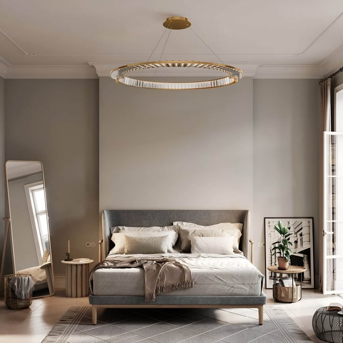Gold-rimmed circular chandelier above a grey upholstered bed in a neutral-toned minimalist bedroom.