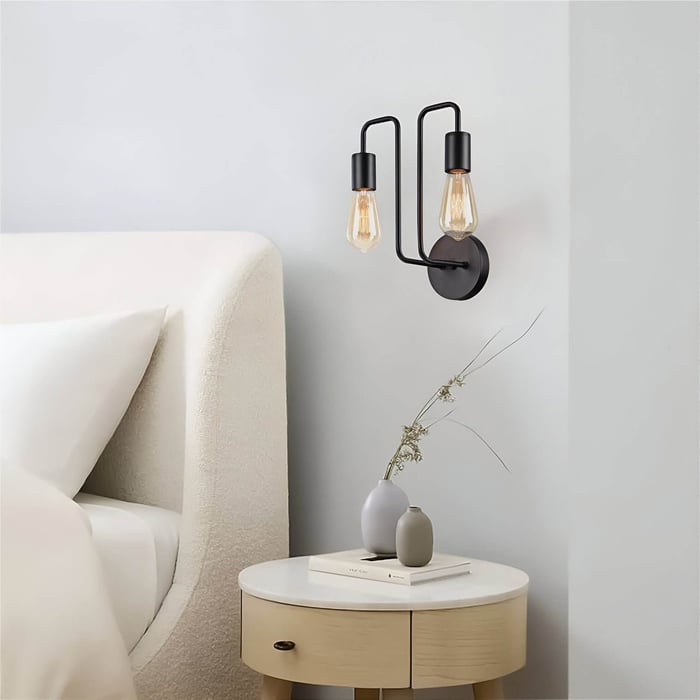 Modern black wall sconce with two exposed Edison bulbs above a minimalist nightstand.
