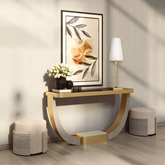 Curved console table with tall gold lamp, abstract art & textured stools in sunlit hallway