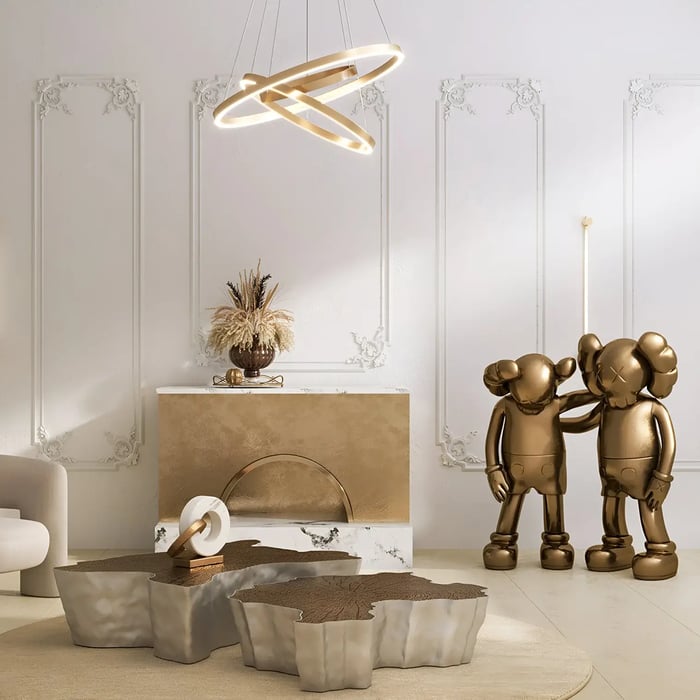 A stylish room with a suspended circular LED light fixture, accented by abstract bronze statues and a contemporary fireplace, all within an ornate walled setting.