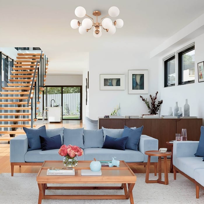 Modern living room lights — Bright open living room with blue sofas and a mid-century modern ceiling light with multiple frosted globes.