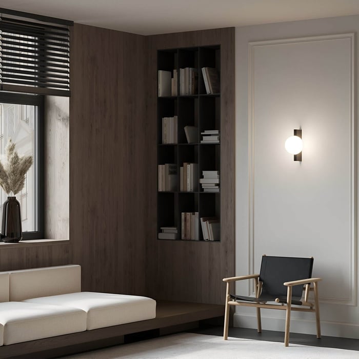 White globe wall sconce mounted on a textured wall beside a modern reading chair and bookshelf.