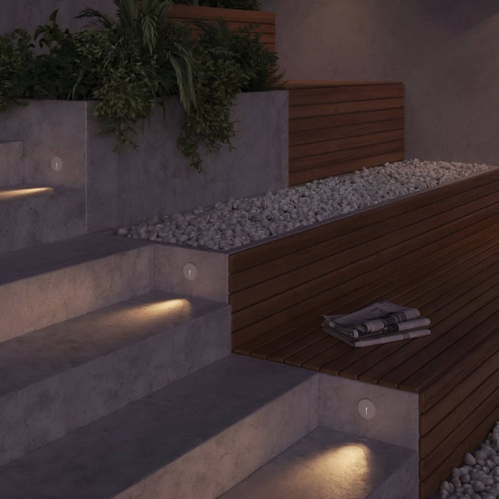 Round recessed wall lights casting downward light on outdoor concrete steps and wood seating with decorative stones.