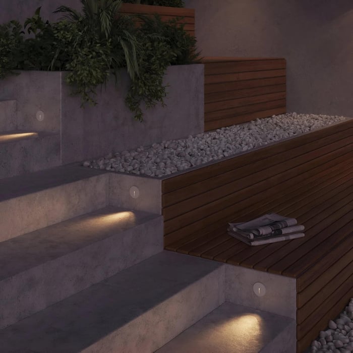 Concrete outdoor steps with small round recessed wall lights casting a soft glow onto each tread beside a timber-clad planter.