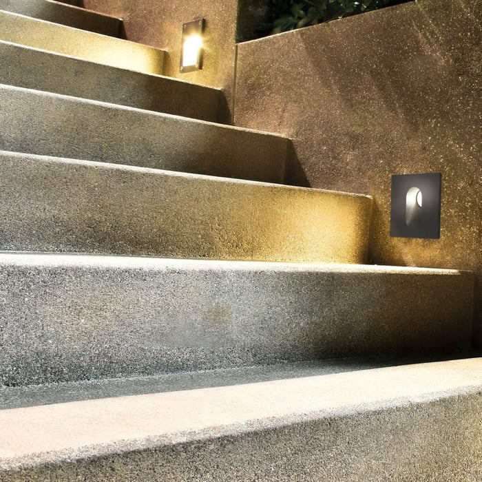 Textured stone staircase with a square wall light washing warm light across the treads for safer night-time footing.