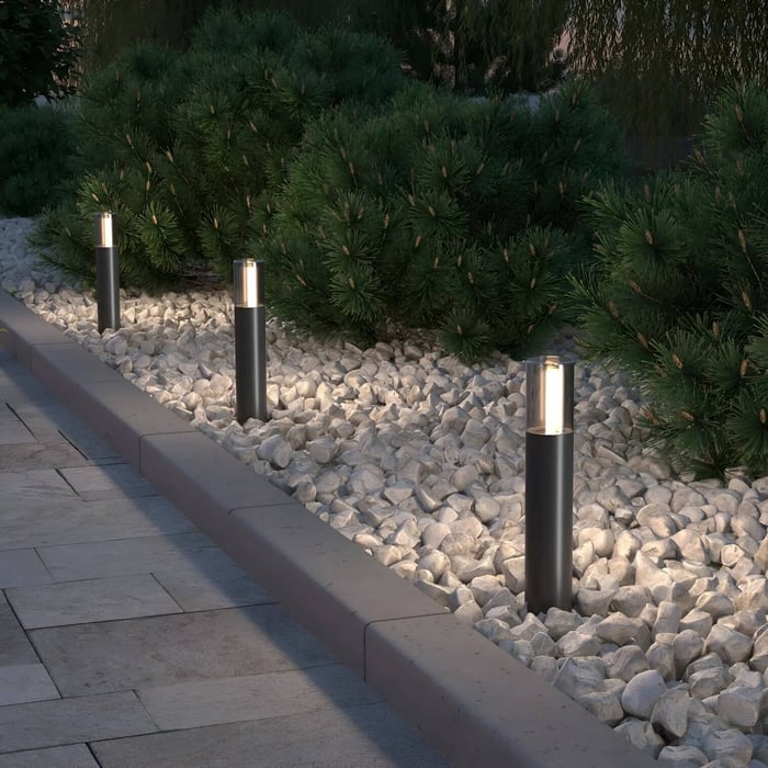 Black bollard lights lined along a stone border beside evergreen shrubs.