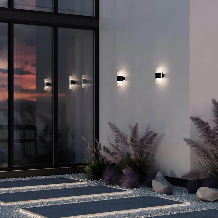 Front porch with open dark door, glowing lantern-style outdoor wall light, bench seating, and greenery.