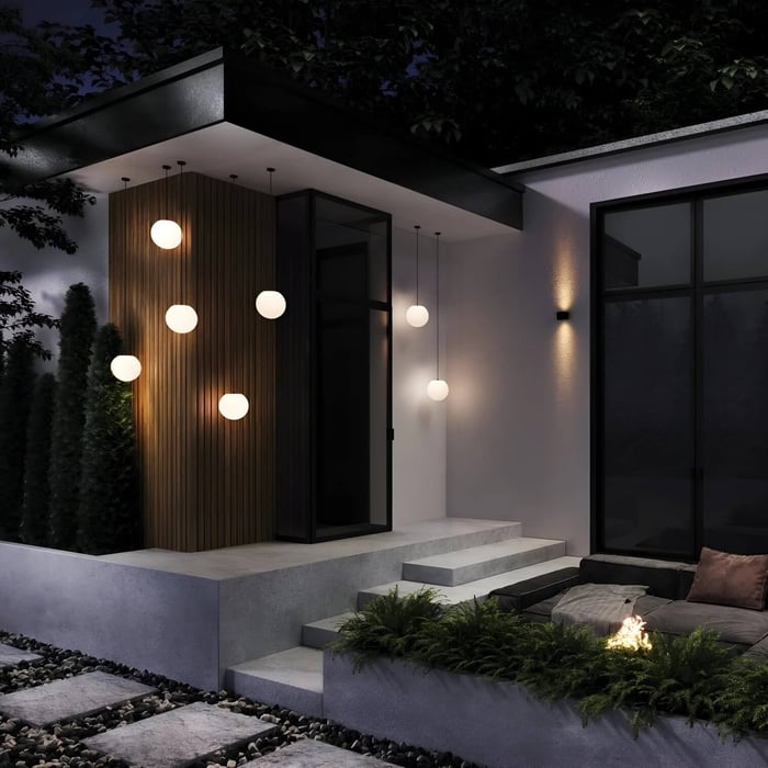 Modern home exterior at night with multiple globe pendant lights clustered beside the front steps.