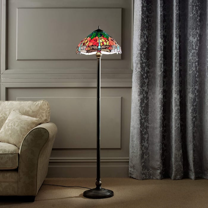 Colorful stained glass Tiffany floor lamp with a floral pattern stands next to a beige armchair and grey damask curtains.