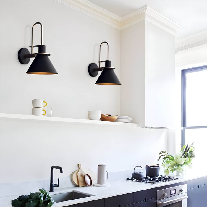 White kitchen wall with matte black cone wall sconces, open shelf, and daylight streaming through a tall window.