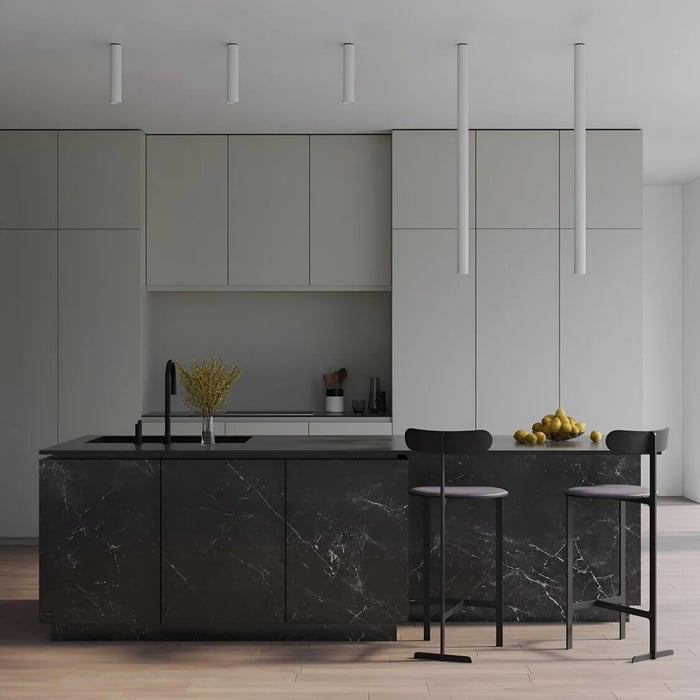 Minimalist modern kitchen with matte gray cabinetry and a black marble island, lit by slim white tube ceiling lights above two bar stools and a bowl of lemons.
