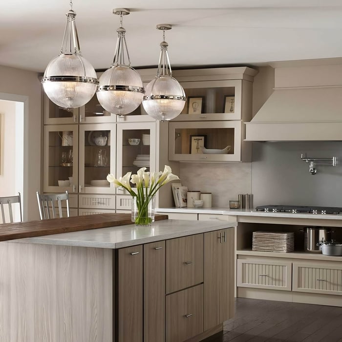 Traditional kitchen with globe pendant lights, wood cabinetry, and a two-tone island topped with marble and fresh white flowers.