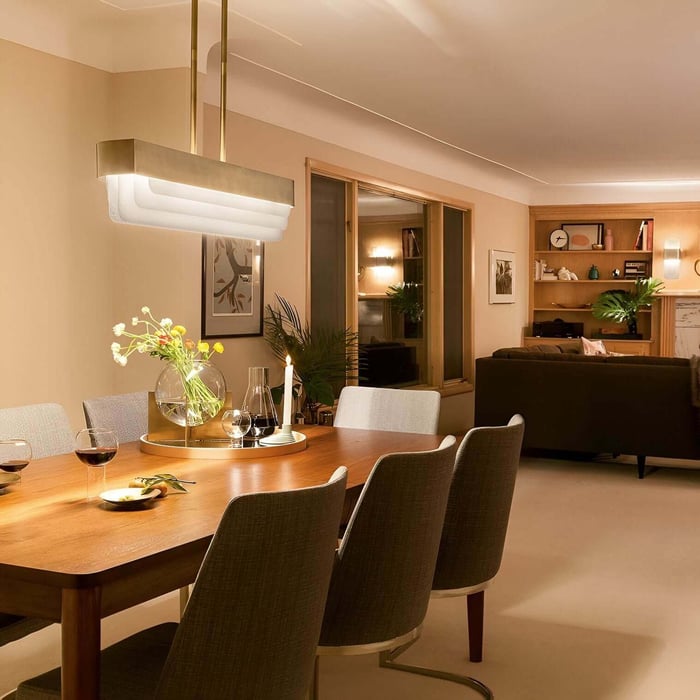 Warm dining room with wooden table, gray chairs, and a sleek rectangular pendant light above the table.