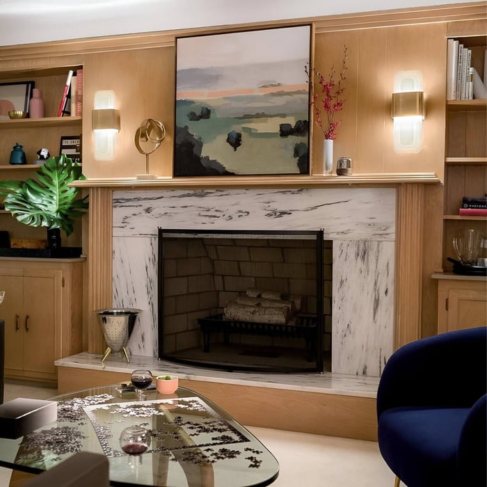 Brass and glass wall lights flanking a fireplace with a marble surround and wooden cabinetry.