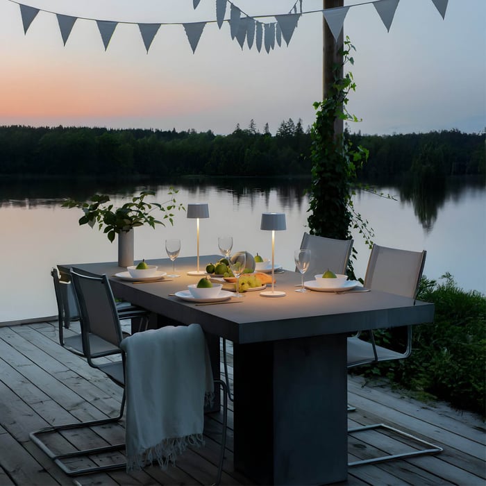 Set of sleek portable table lamps on an outdoor lakeside dining table at sunset with minimalist place settings.