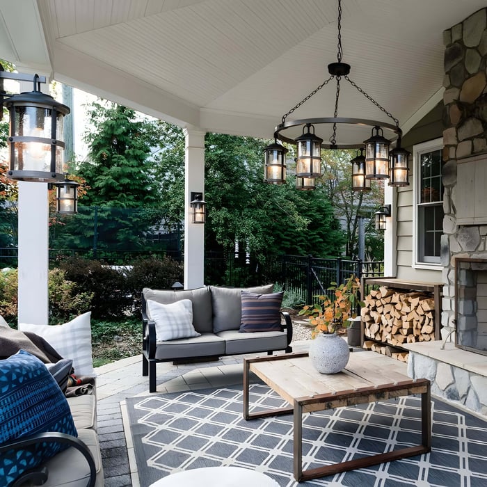 Cozy covered patio with lantern-style chandelier, wall sconces, cushioned sofas, and stone fireplace.
