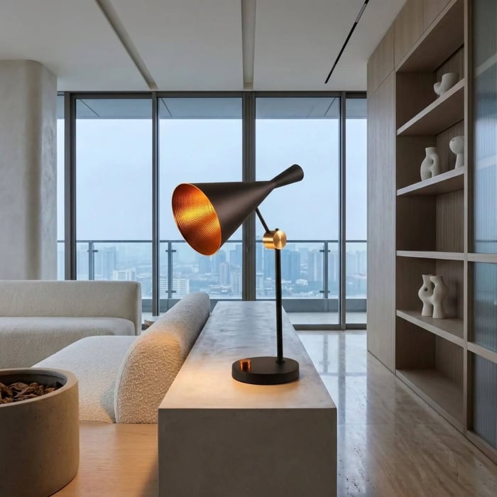 A sleek black conical table lamp with a glowing gold interior sits on a concrete console in a modern high-rise living room..