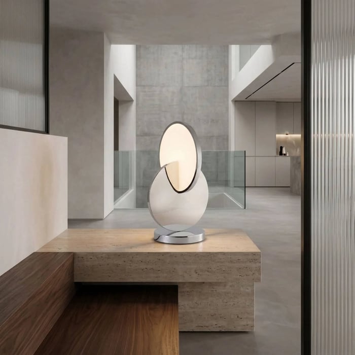 Minimalist chrome lamp with overlapping circular disks on a stone ledge in a concrete modern interior.