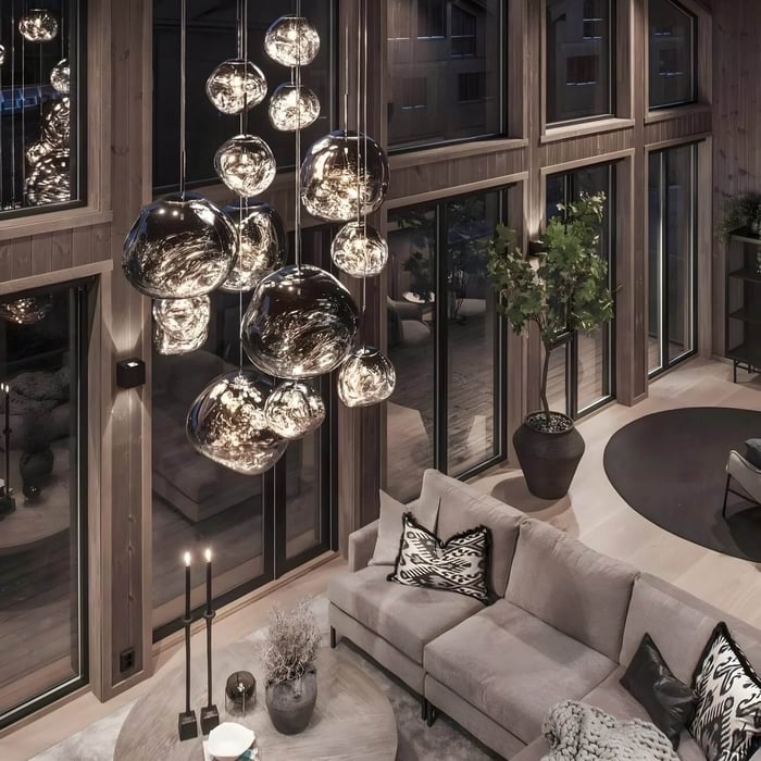 Double-height living room with cascading bubble glass pendant lights, grey sectional, and tall windows with black framing.