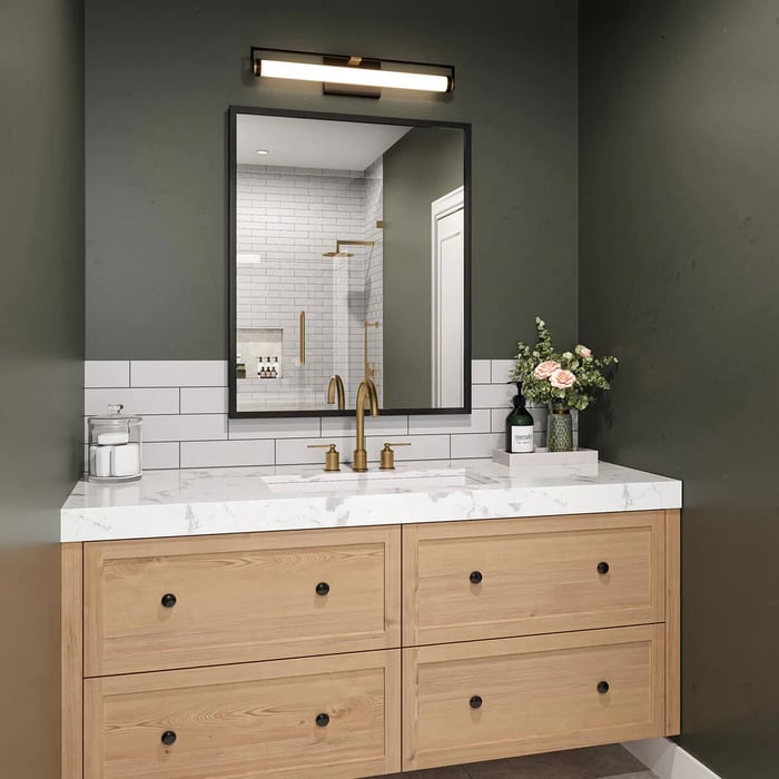 Vanity light above a black-framed bathroom mirror over a wood drawer unit and marble countertop.