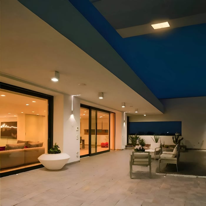 Covered terrace with small surface-mounted downlights lighting a seating area beside large sliding glass doors at night.
