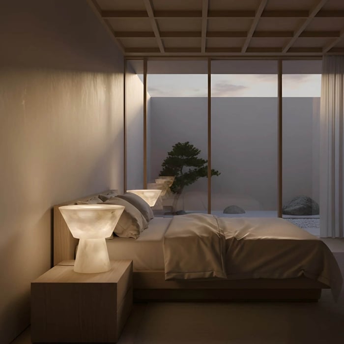 Minimalist bedroom at dusk with sculptural bedside lamps and a courtyard view through large glass windows.