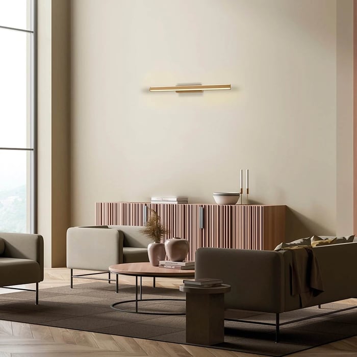 Minimalist living room with neutral sofas and round coffee table, ribbed blush-wood sideboard and brass linear wall sconce above.