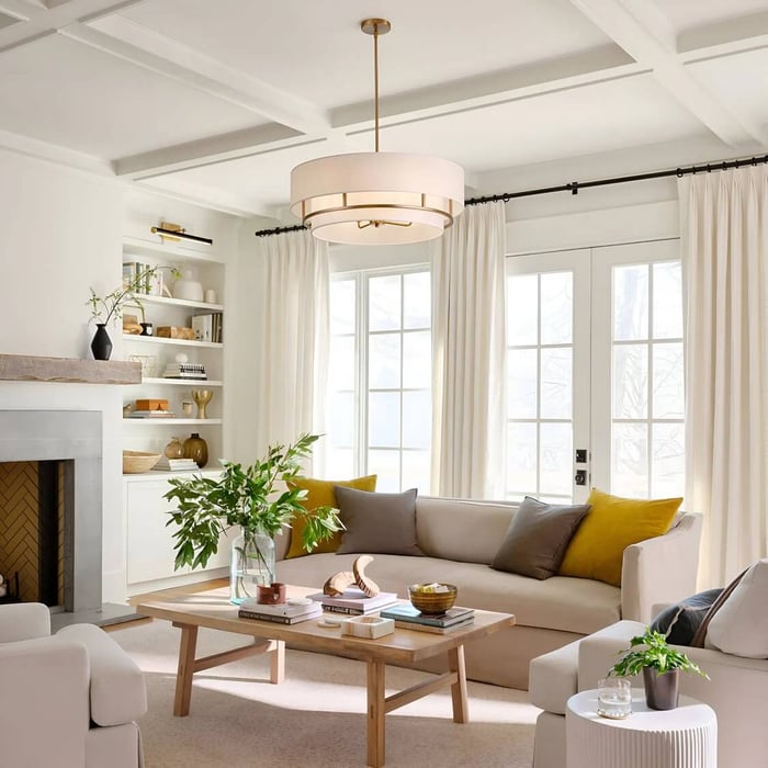 Bright transitional living room with a white drum pendant light, coffered ceiling, neutral sofa, light wood coffee table, and sunny windows with soft curtains.