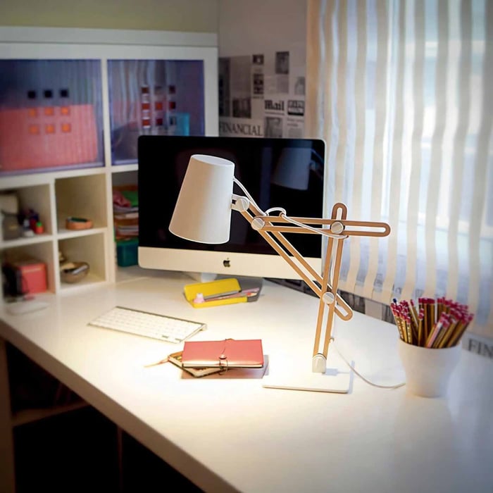 White adjustable task lamp on a clean desk setup with a computer, notebook, and pencil pot by a window.