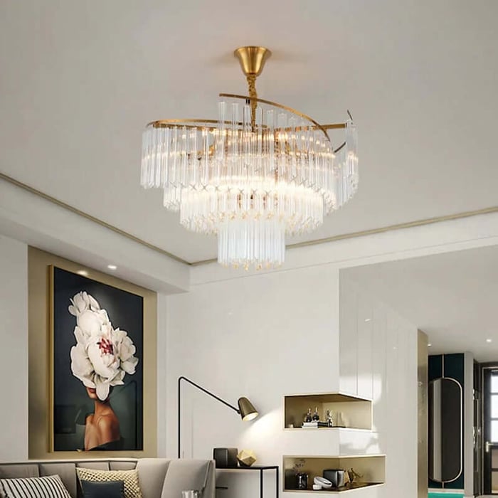 Modern living room with a gold spiral crystal chandelier on the ceiling, above a grey sofa, wall art of a flower portrait, and built-in white shelving.
