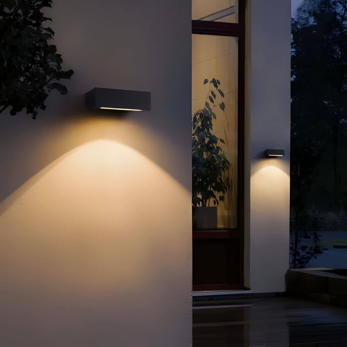 Rectangular outdoor wall light casting a warm downward beam beside a front door.