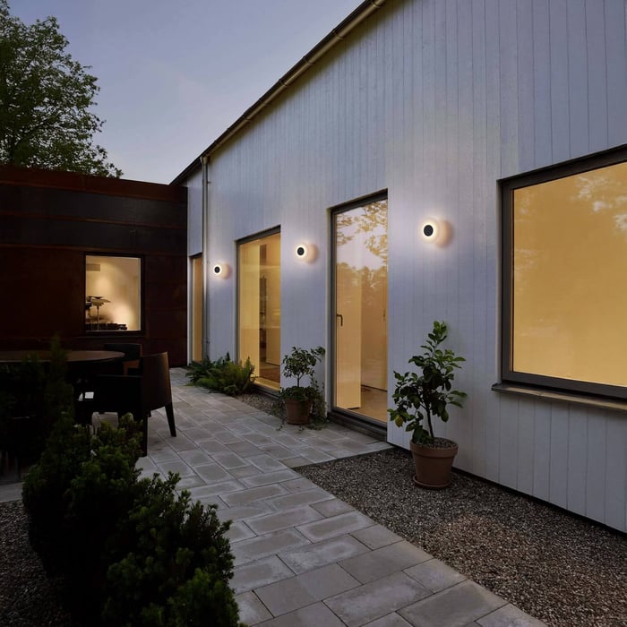 Modern outdoor walkway with minimalist circular wall lights illuminating a white exterior facade at dusk.