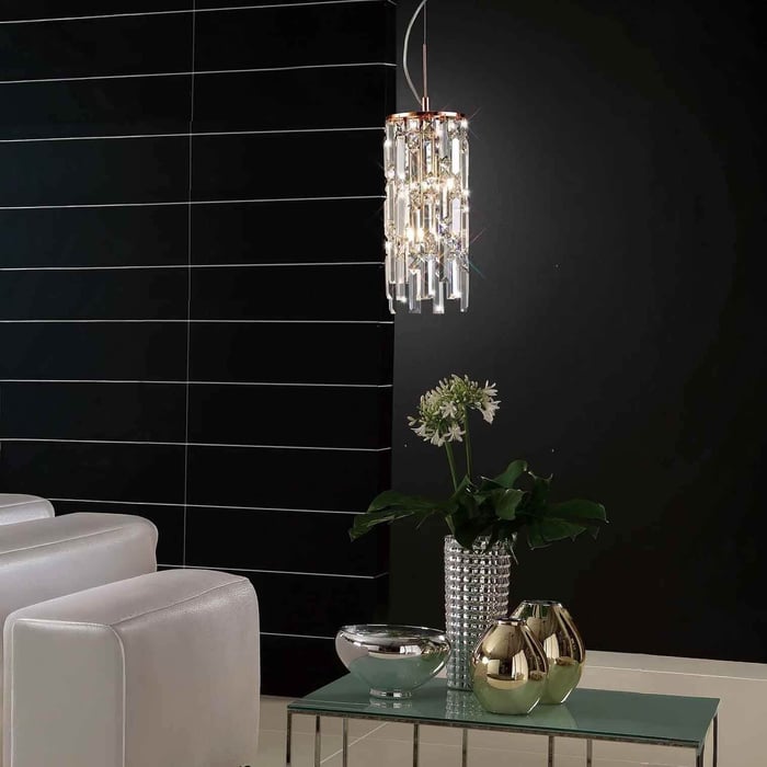 Bathroom corner with a crystal pendant light hanging over a glass table and décor against a dark tiled wall.