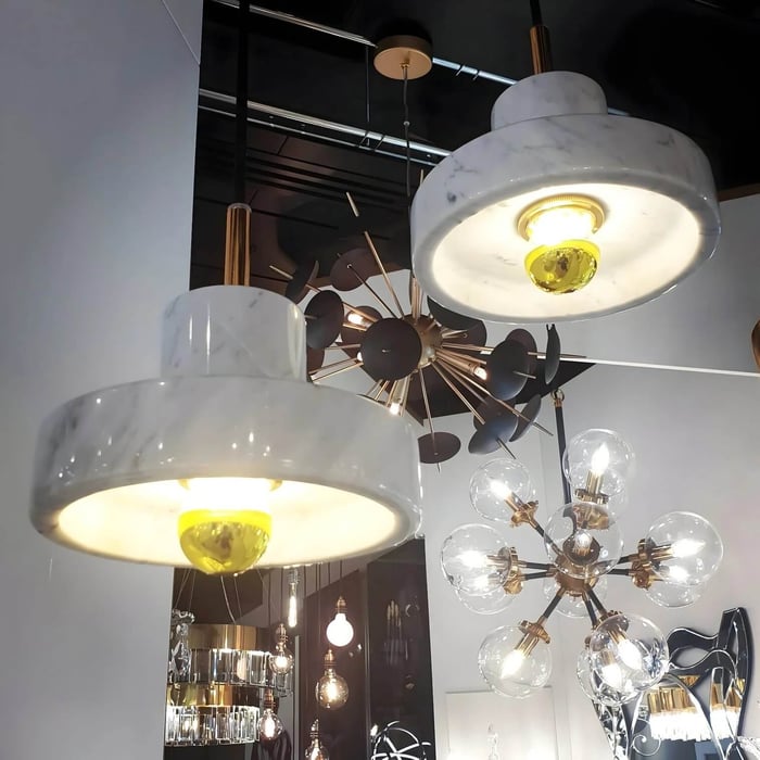 Close-up of modern marble pendant lights with white stone shades and gold accents, displayed alongside decorative glass globe and starburst chandeliers in a contemporary showroom.