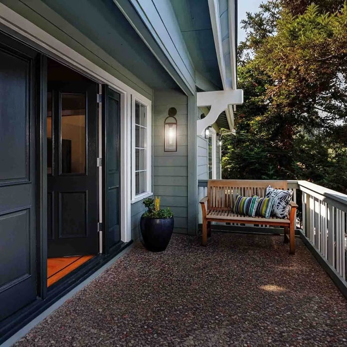 Modern home exterior with glass doors and two minimalist outdoor wall lights along a gravel walkway at sunset.