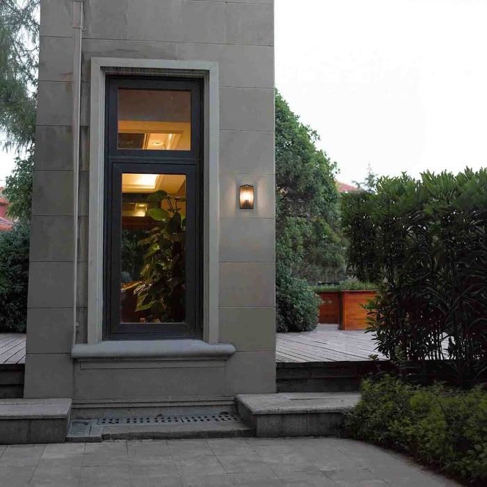 House siding with large windows, bright flower garden, and a geometric outdoor wall light casting a triangular beam.