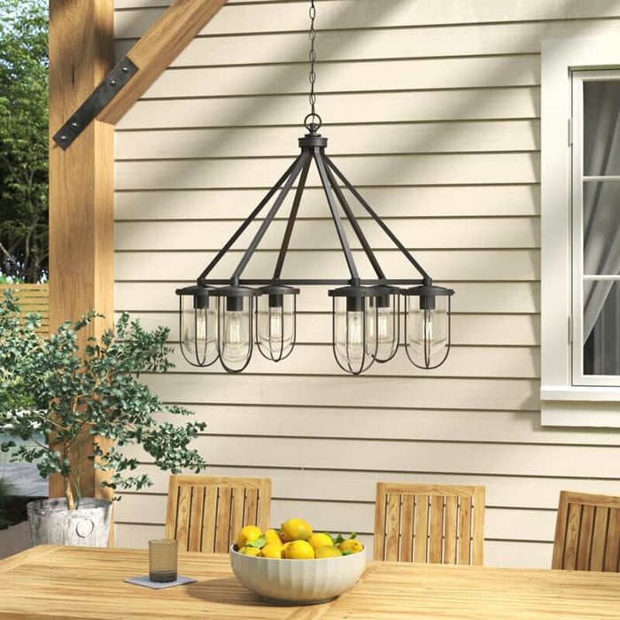 Black metal frame outdoor chandelier with clear glass shades hanging above a wooden outdoor dining table.