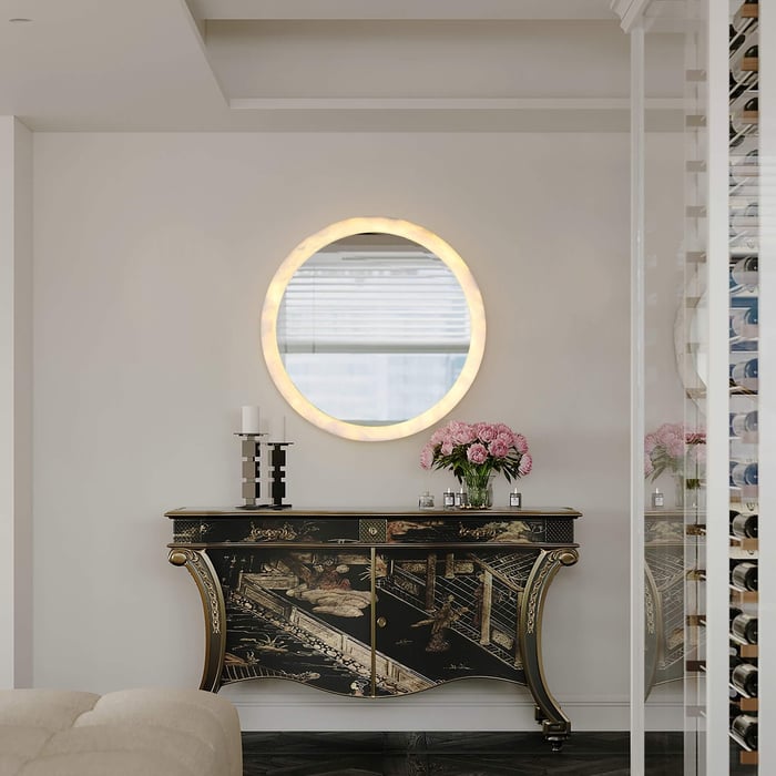 Circular alabaster mirror mounted above a decorative antique console with floral arrangement.
