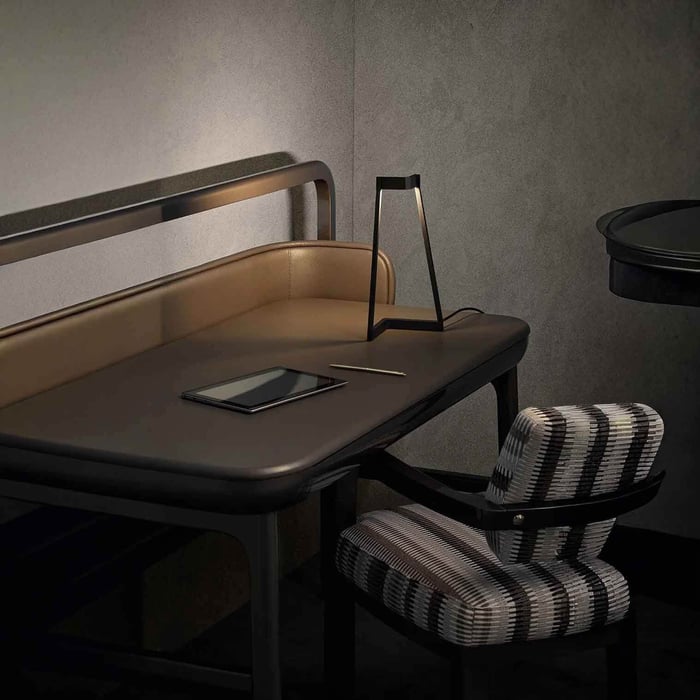 Moody workspace with a slim black LED table lamp on a dark desk beside a tablet and pencil.