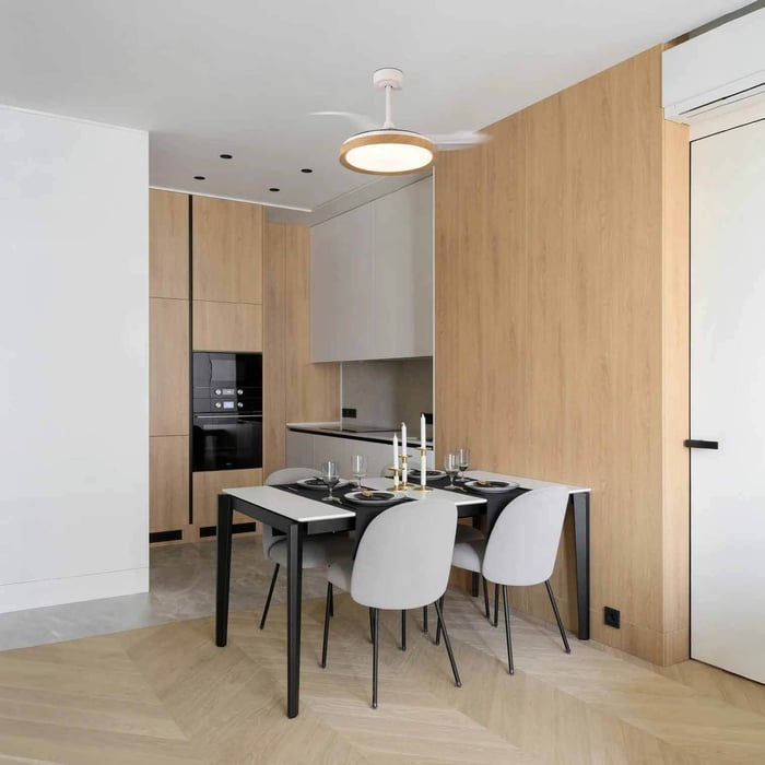 Minimalist dining area with light wood wall panels, a black dining table set for four, and a white ceiling fan with an integrated round LED light above the table.