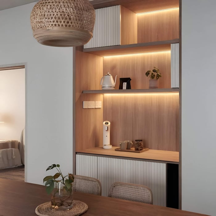 Built-in wooden shelving with warm LED strip lighting under each shelf, styled with a kettle, cups, and small plant above a dining table.