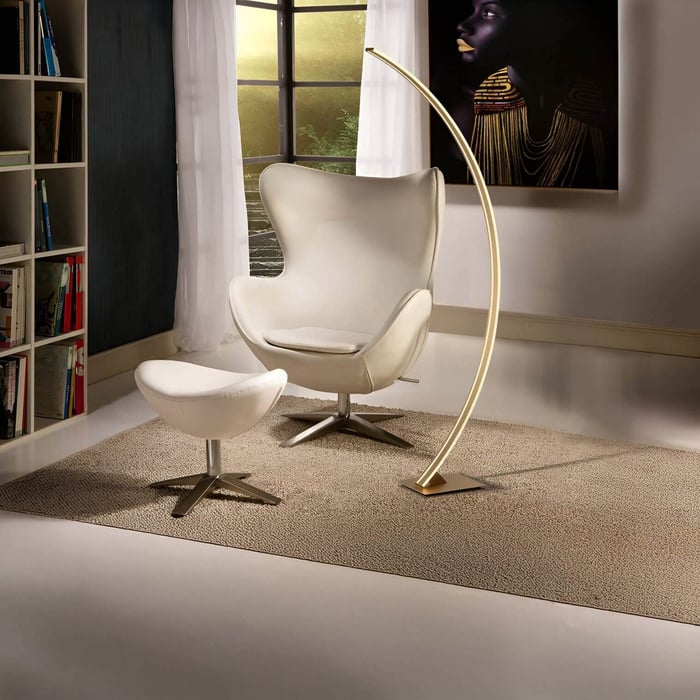 Elegant curved LED floor lamp glowing warmly beside a white lounge chair and ottoman.