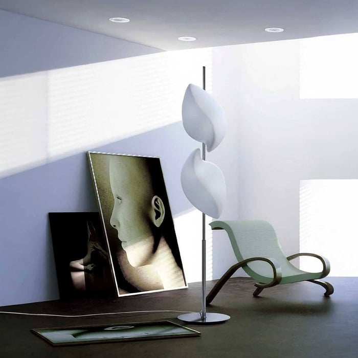 White sculptural floor lamp in a bright minimalist room with framed artwork leaning against the wall.