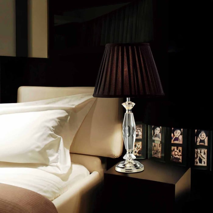 Faceted crystal traditional table lamps with a black pleated shade on a bedside table beside a bed with white bedding.