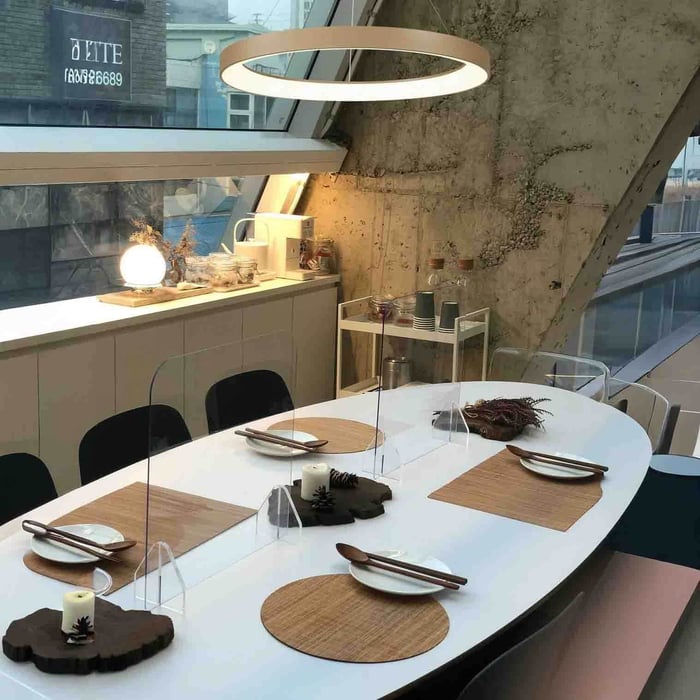 Minimal circular ring pendant light above an oval dining table in a modern loft with slanted glass windows and concrete walls.