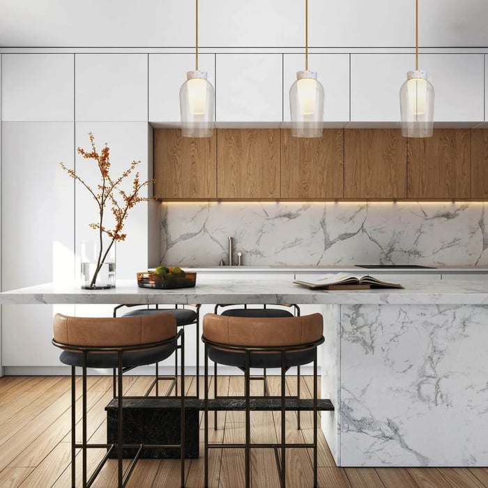 Airy modern kitchen showcasing a marble waterfall island, wood upper cabinets, and three clear glass pendants above leather stools.