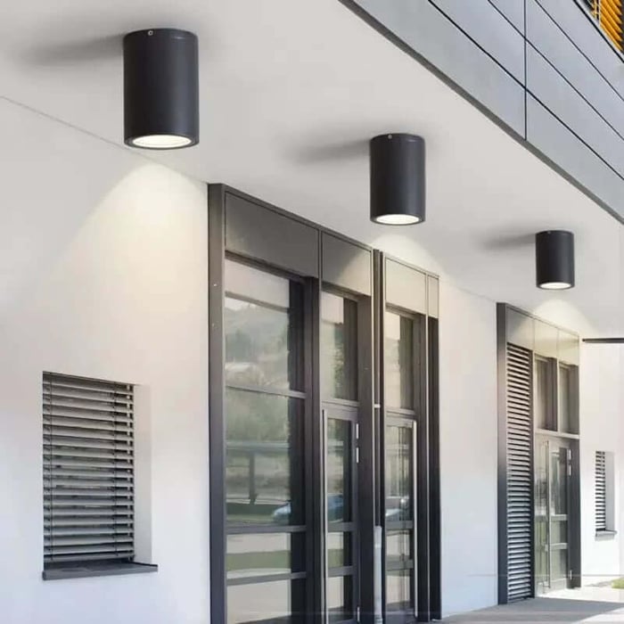 Black cylindrical outdoor downlights fitted under a modern building overhang above windows.