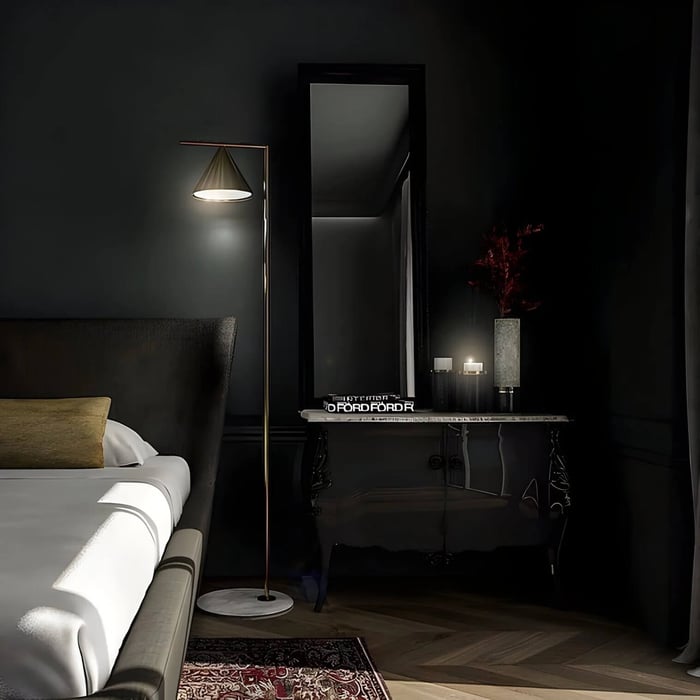 Brass floor lamp with a cone shade beside a bed in a dark, moody bedroom setting.
