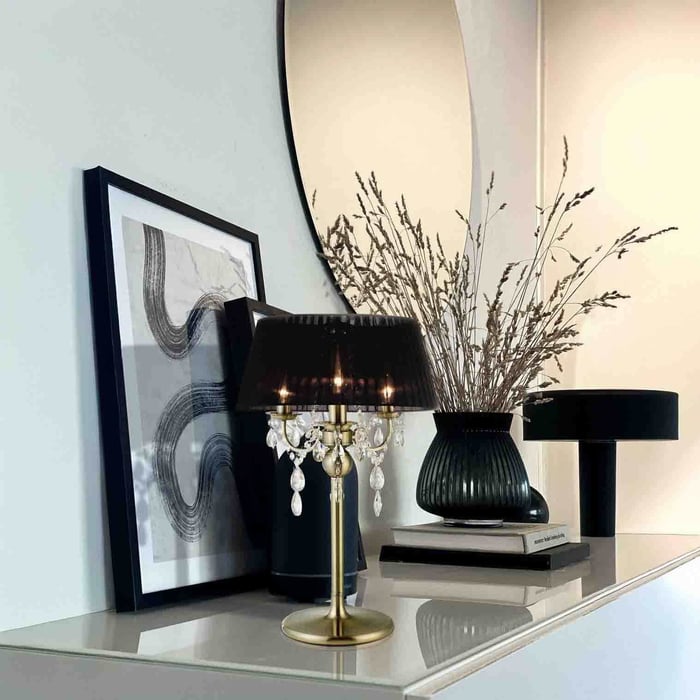 Black shade table lamp with hanging crystal drops on a glossy console styled with framed art, books, and a vase.